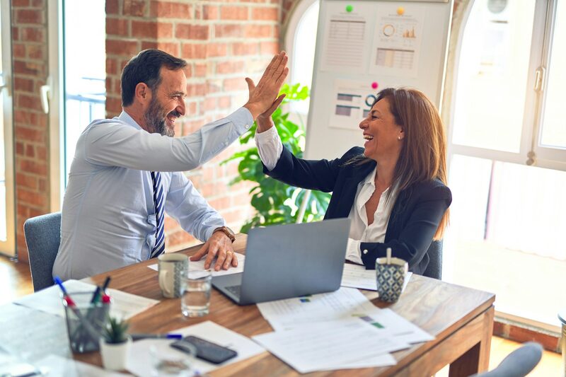Two colleagues celebrating a campaign result with a high five at their desk